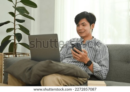 Cheerful asian man hand holding mobile phone and looking at laptop screen. People, technology and lifestyle concept