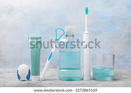 Electronic ultrasonic toothbrush, mouthwash, floss, tongue cleaner and toothpaste on blue textured background. Items for dental care and caries prevention in the bathroom. Dentistry concept. Copy spac