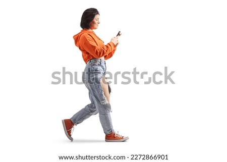 Full length profile shot of a gen z female using a smartphone and walking isolated on white background