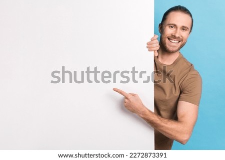 Photo of cheerful positive guy dressed beige t-shirt pointing finger white placard emtpy space isolated blue color background