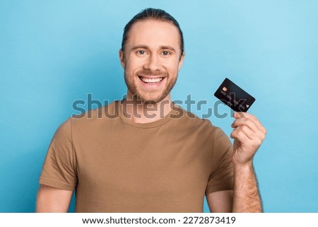 Photo of young smile optimistic cheerful promoter guy wear brown t-shirt hold plastic payment wireless card shopping isolated on blue color background