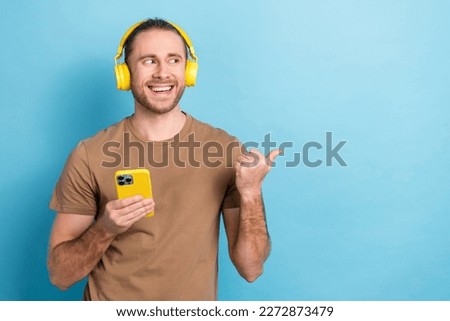 Photo of cheerful handsome guy hold smart phone look indicate finger empty space isolated on blue color background