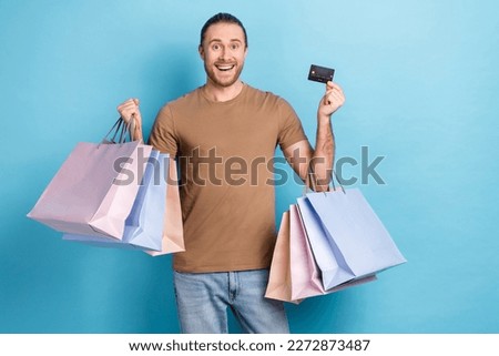Photo of adorable excited guy dressed beige t-shirt holding shoppers rising bank card isolated blue color background