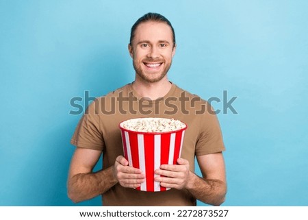 Photo of cheerful positive guy dressed beige t-shirt watching movie eating pop corn isolated blue color background