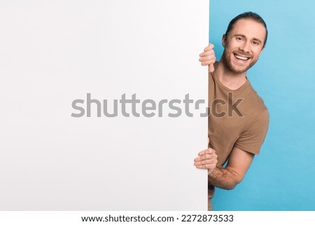 Portrait of satisfied young man beaming smile peeking behind empty space blank isolated on blue color background Royalty-Free Stock Photo #2272873533