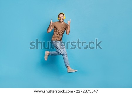 Full length photo of funky cool guy dressed beige t-shirt jumping listening hard rock gesture isolated blue color background