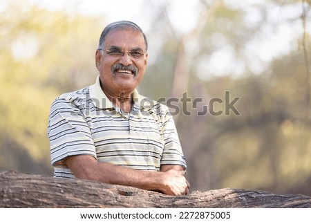 Happy senior man with arms crossed at park Royalty-Free Stock Photo #2272875005