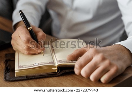 A businessman sits at a table and makes notes in a notebook. Close-up.