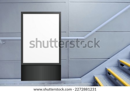 Blank white vertical digital display in front of painted concrete wall, beside flight of stairs. Template for mock up of advertising poster.