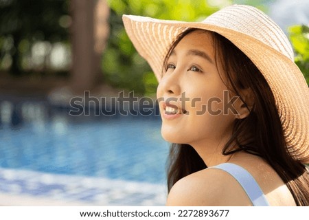 Happy smiling relaxed summer woman wearing bikini swimsuit with hat at swimming pool, looking up