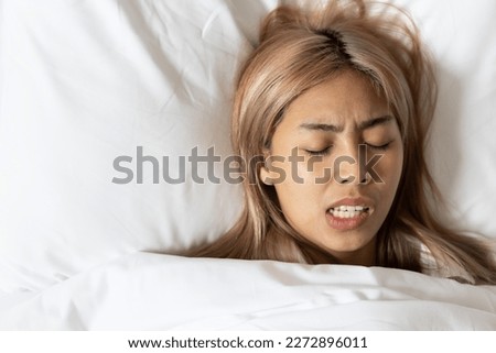 Tired and stressed Asian woman with colored hair sleeping, having bad dream, nightmare with bruxism or grinding teeth Royalty-Free Stock Photo #2272896011