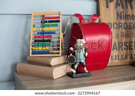 Red backpack, Books, abacus, figurine hare on wooden table. Written on the board Toulouse, Dijon, Bourges, Paris. Modern interior study room with Workplace for school child. Desk in child bedroom. 