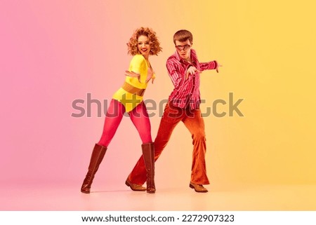 Disco style. Young emotional man and woman, professional dancers in retro clothes dancing dance over pink-yellow background. American culture, 1970s, 1980s fashion, music concept Royalty-Free Stock Photo #2272907323