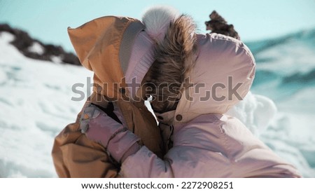 Little girl kisses her baby sister in snowy mountains in winter