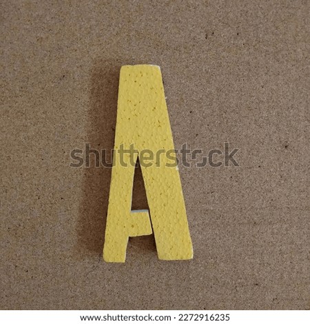 Photo of the letter A in white, three-dimensional shape textured on a cardboard background