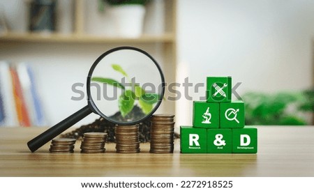 The abbreviations R and D stand for research and development.  The initials rested on a green wooden block with a coin, a magnifying glass and a sapling. Royalty-Free Stock Photo #2272918525