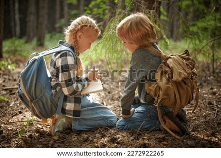 Two curious active kids in denim clothes with backpacks sit in a forest during their nature expedition. Adventure and nature exploring for kids. Active children. Royalty-Free Stock Photo #2272922265