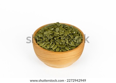 green peeled pumpkin seeds in small brown wooden cup, isolated on white background