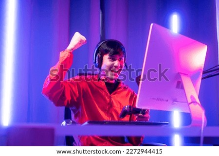 Professional gamer casting podcast walkthrough review. Young asian man sitting on chair with computer pc and microphone. Happy male Streamer wearing headphone playing game online in room neon light Royalty-Free Stock Photo #2272944415