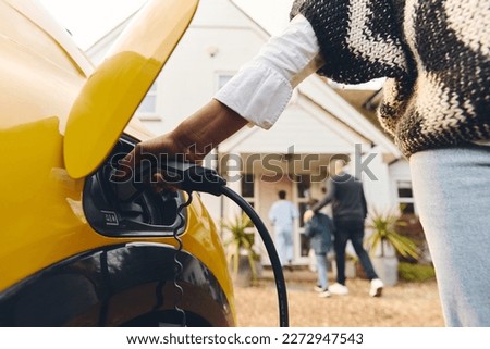 Woman plugging electric charger into car Royalty-Free Stock Photo #2272947543
