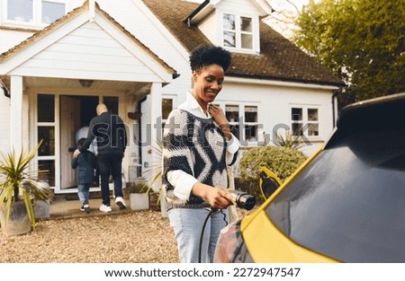 Woman plugging in electric charger into car Royalty-Free Stock Photo #2272947547