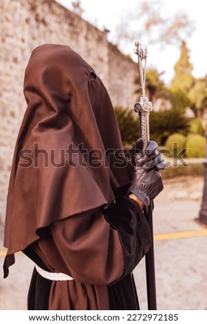Nazarene dressed in brown tunic and covered face walking and dragging a large cross at night under the moon through an old Spanish city. Royalty-Free Stock Photo #2272972185