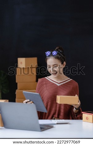 Asian female business owner uses laptops and tablets to take and verify online orders to prepare boxes. Packing products for delivery to customers, SME business concept, e-commerce, online shopping ve