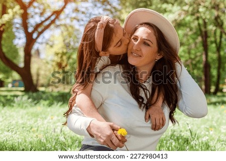 Girl kisses mother on cheek hugging while sitting on grass in spring park giving flower. Family relaxing outdoors. Mothers day. Close up