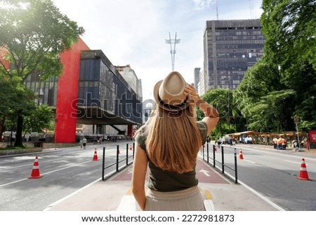 Visiting Sao Paulo City, Brazil. Rear view of beautiful tourist woman with hat walking along Paulista Avenue, Sao Paulo, Brazil. Royalty-Free Stock Photo #2272981873