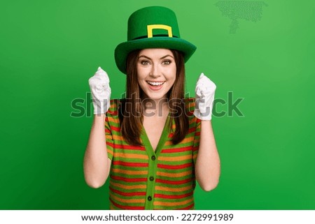 Portrait of funky delighted girl toothy smile raise fists wear gloves hat isolated on green color background