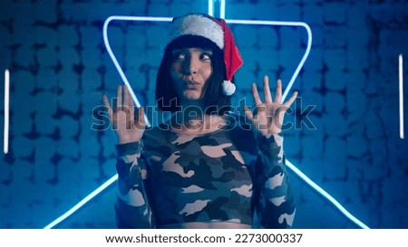 Cheerful lady in Santa Claus hat dances energetically and moves fingers against futuristic neon light closeup slow motion