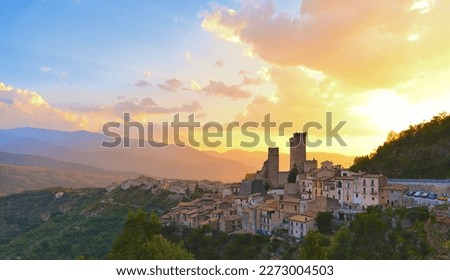 Pacentro (Italy) - Panoramic view on old small medieval town with stone houses and roofs and castle towers with city of Sulmona and warm sunset in background, province of L'Aquila, Abruzzo region 