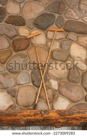 Two antique polo mallets in a criss-cross position standing on the wooden mantel of a stone fireplace Royalty-Free Stock Photo #2273009283