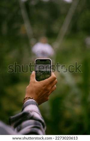 Man takes a picture on a phone of a woman on a swing in the jungle, vacation Bali.