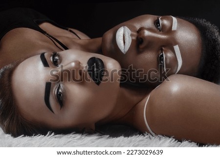Black and blonde model fashion girls with contrast artistic makeup in studio light