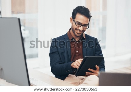 Office, happy Indian man at desk with tablet and computer, reading good news email or successful sales report online. Business, smile and communication with internet, social media or research on web. Royalty-Free Stock Photo #2273030663