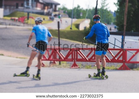Athletes  ride roller skis on asphalt track, group of ski rollers in helmet, cross-country skiing with roller ski in summer sunny day, sportsmen ski-rollers riding, biathlete training 