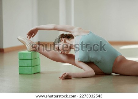 Beautiful teen girl, professional female ballerina training in ballet school on daytime. Sitting on twine and doing stretching exercises. Classical ballet, dance art, education, beauty, choreography