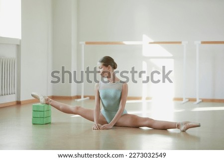 Tender beautiful teen girl, ballerina training in ballet school on daytime. Stretching exercises, sitting on twine. Concept of classical ballet, dance art, education, beauty, choreography