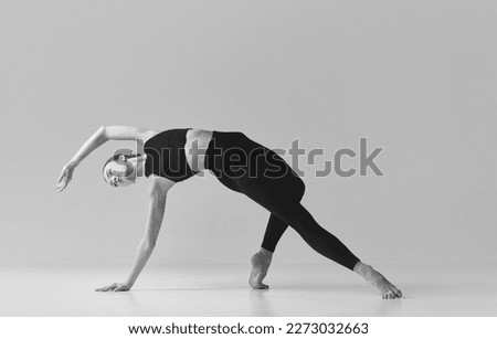 Flexibility. Black and white photography. Young slim, fit girl training, doing stretching exercises over studio background. Concept of sport, body care, beauty, fitness, active lifestyle. Ad