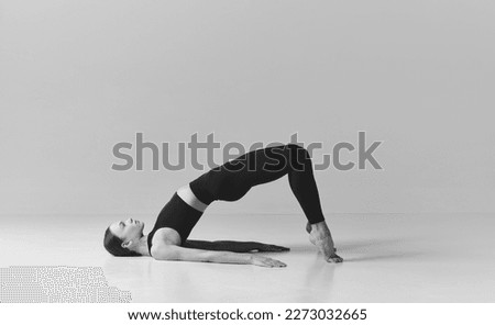 Slim fit body. Black and white photography. Young girl doing stretching, press exercises, training over studio background. Concept of sport, body care, beauty, fitness, active lifestyle. Ad