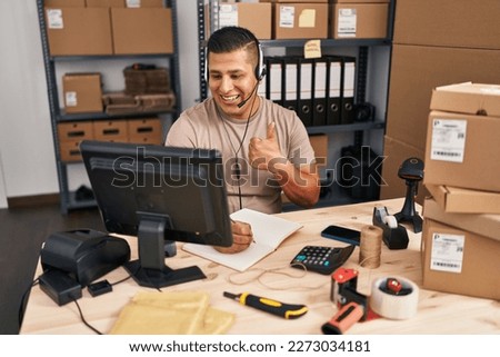 Hispanic young man working at small business ecommerce smiling happy and positive, thumb up doing excellent and approval sign 