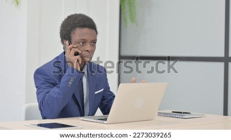 Displeased African Businessman Talking Angrily on Smartphone at Work