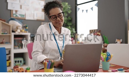 African american woman preschool teacher using laptop sitting on chair at kindergarten