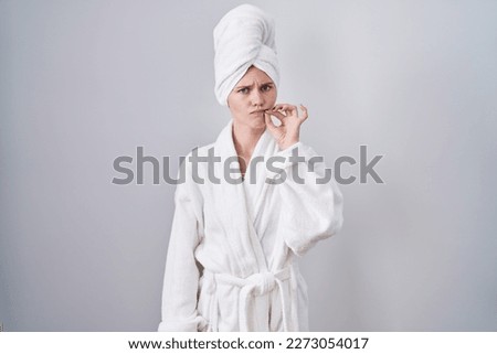 Blonde caucasian woman wearing bathrobe mouth and lips shut as zip with fingers. secret and silent, taboo talking 