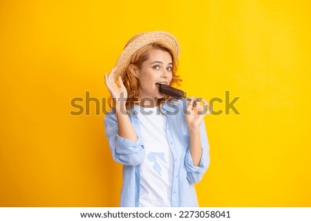 Portrait of beautiful woman eating ice cream on orange yellow background. Girl in summer hat eating chocolate popsicle ice pop. Happy excited expression female portrait.