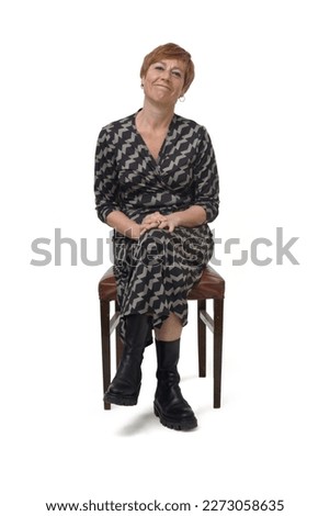 front view a woman in dress and boots sitting on chair cross legged looking at camera on white background Royalty-Free Stock Photo #2273058635