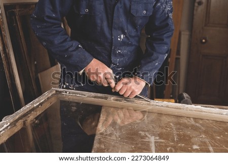 Carpenter renovating old wooden sash windows  -  removing old patty and scraping paint from the woodwork. Royalty-Free Stock Photo #2273064849