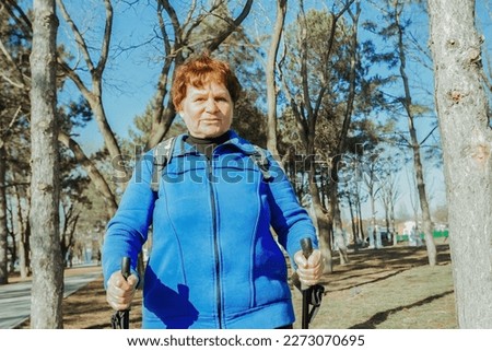 an elderly active woman walks in the park on Scandinavian sticks. Healthy lifestyle of adult women.