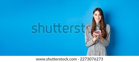Beautiful girl holding birthday cake and celebrating, wishing happy bday and smiling, standing against blue background.
